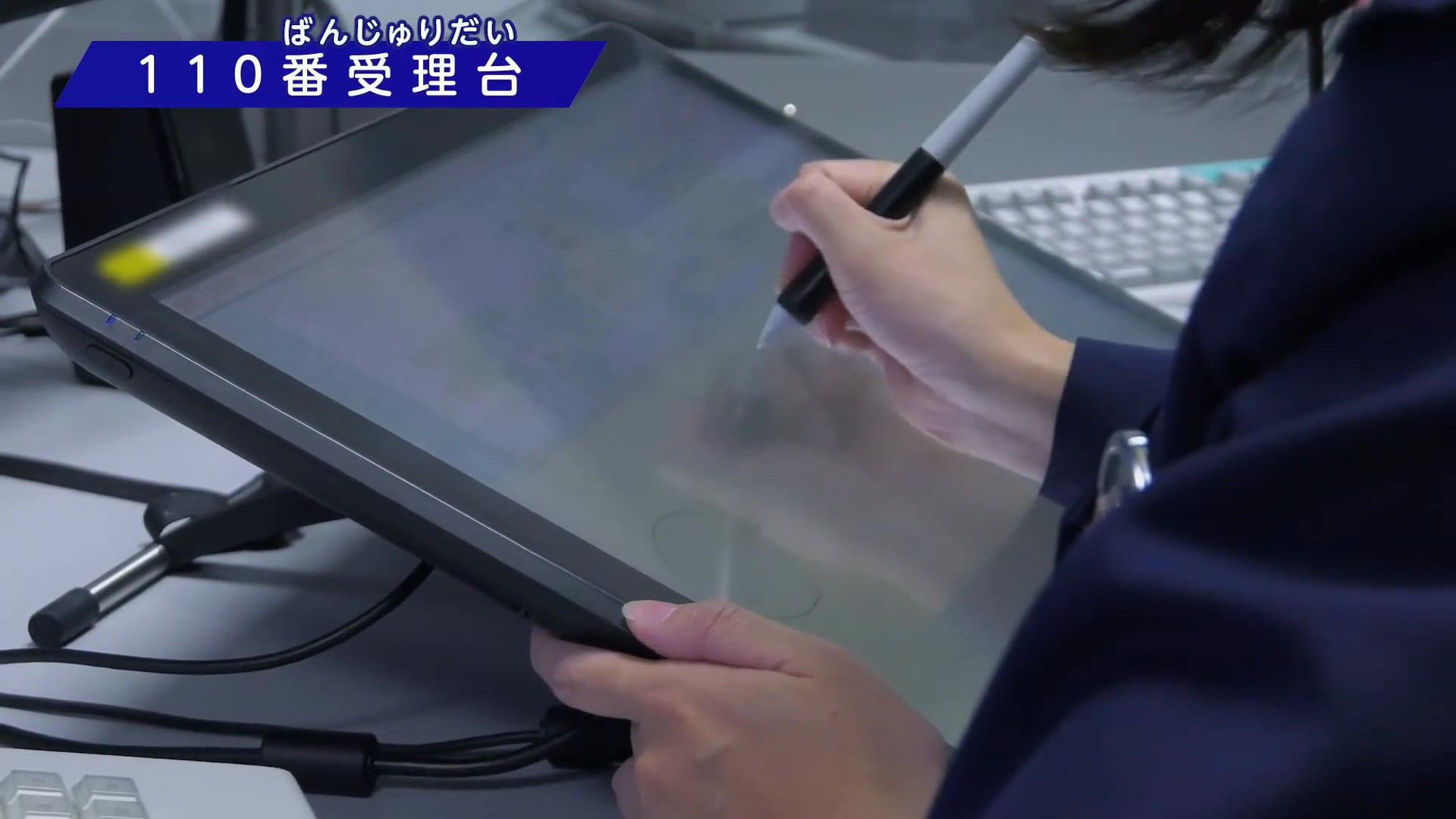 110番受理台の職員が通報を受けながらタブレット端末にメモしている写真