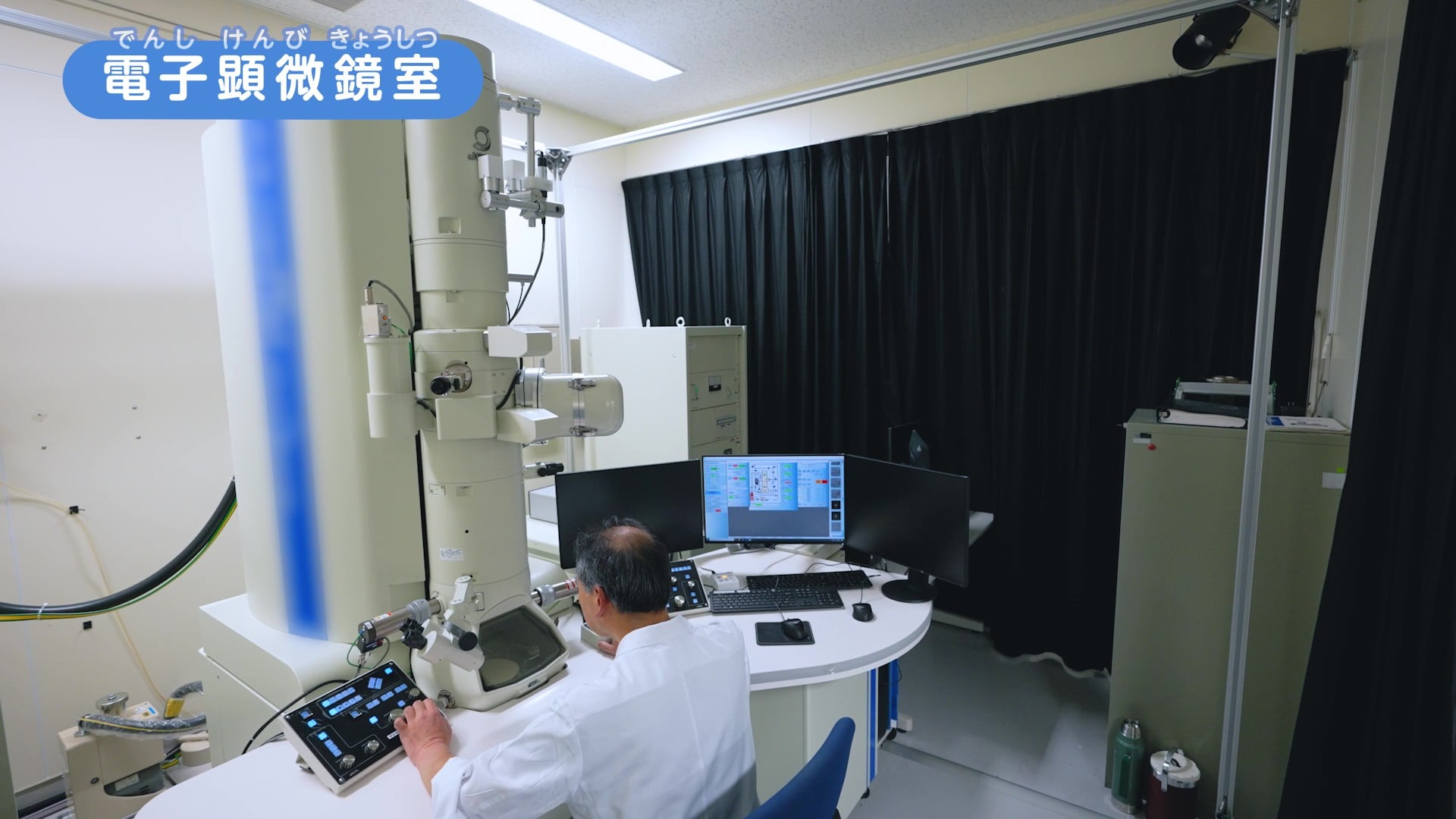 電子顕微鏡室で電子顕微鏡を使ってウイルスをチェックしている写真